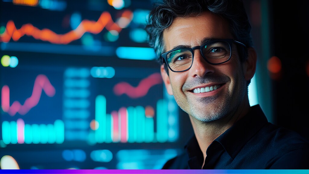 homem caucasiano de óculos, sorridente com paineis ao fundo cheio de gráficos de desempenho