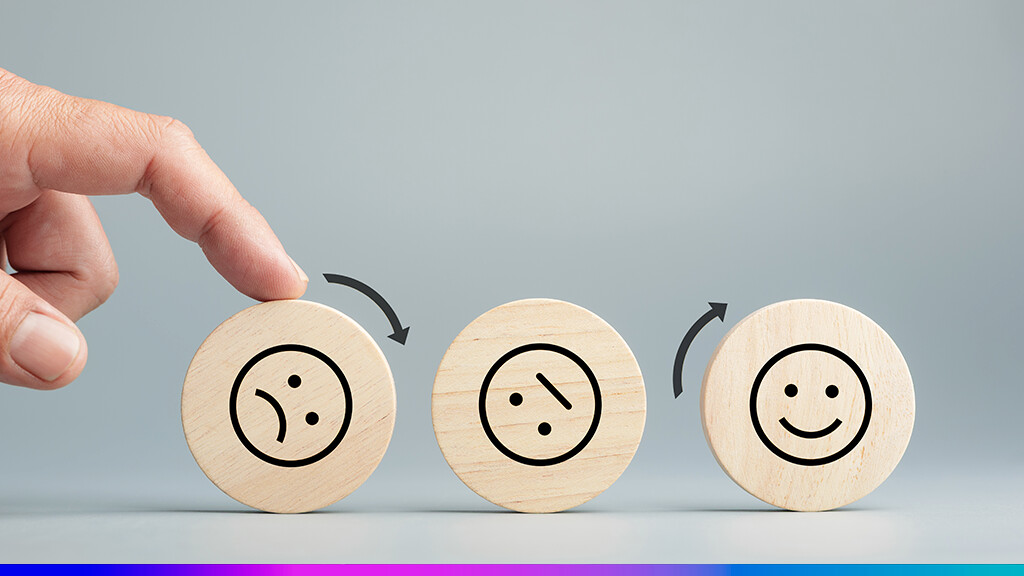 Mão movendo peça de madeira com rostos que representam diferentes níveis de satisfação do cliente, simbolizando a melhoria da experiência por meio da comunicação omnichannel.