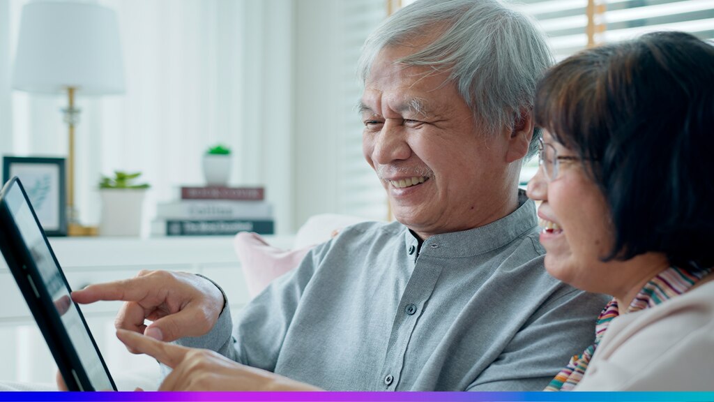 Casal de idosos sorrindo enquanto utiliza um tablet, representando o uso da tecnologia e da transformação digital na área da saúde